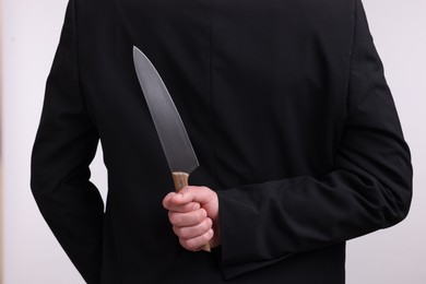 Photo of Businessman holding knife behind his back on white background, closeup