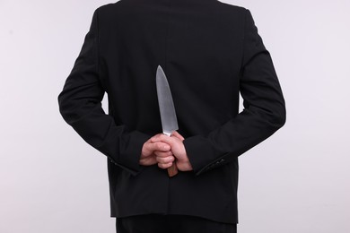 Photo of Businessman holding knife behind his back on white background, closeup