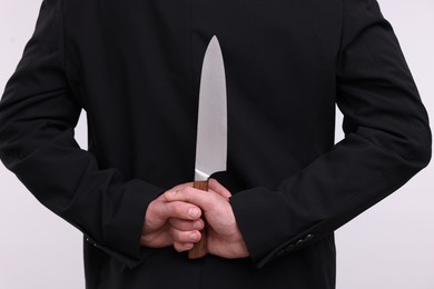 Photo of Businessman holding knife behind his back on white background, closeup