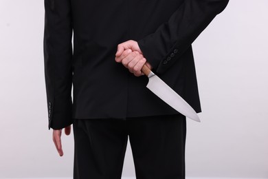 Photo of Businessman holding knife behind his back on white background, closeup