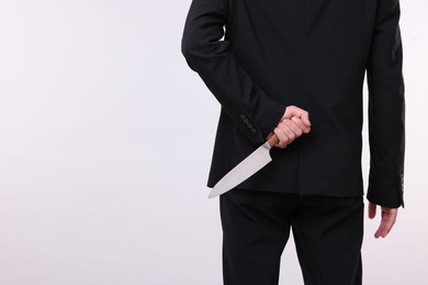 Photo of Businessman holding knife behind his back on white background, closeup. Space for text