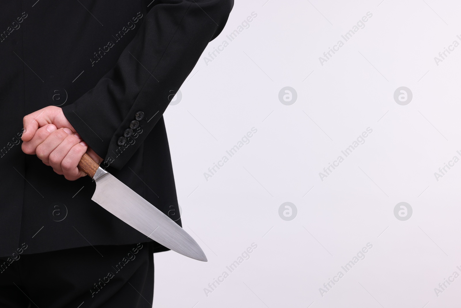 Photo of Businessman holding knife behind his back on white background, closeup. Space for text