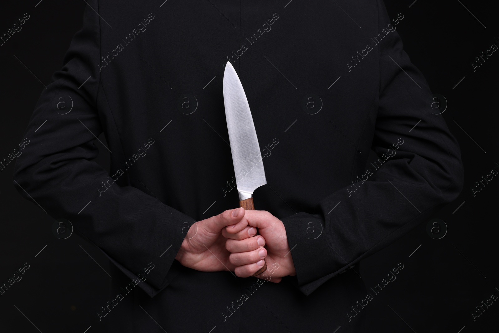 Photo of Businessman holding knife behind his back on black background, closeup