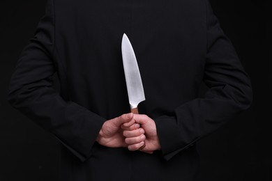 Photo of Businessman holding knife behind his back on black background, closeup