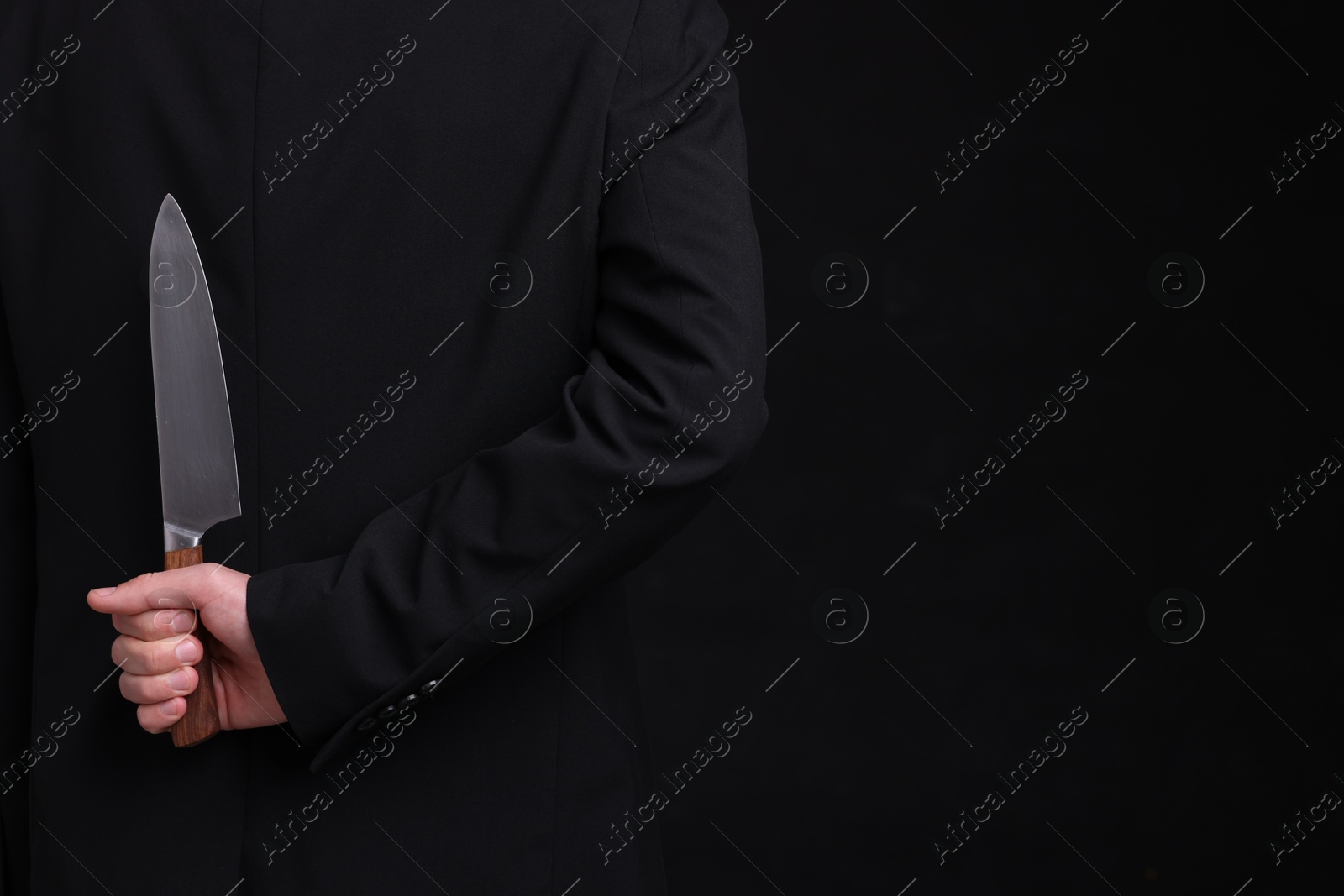 Photo of Businessman holding knife behind his back on black background, closeup. Space for text