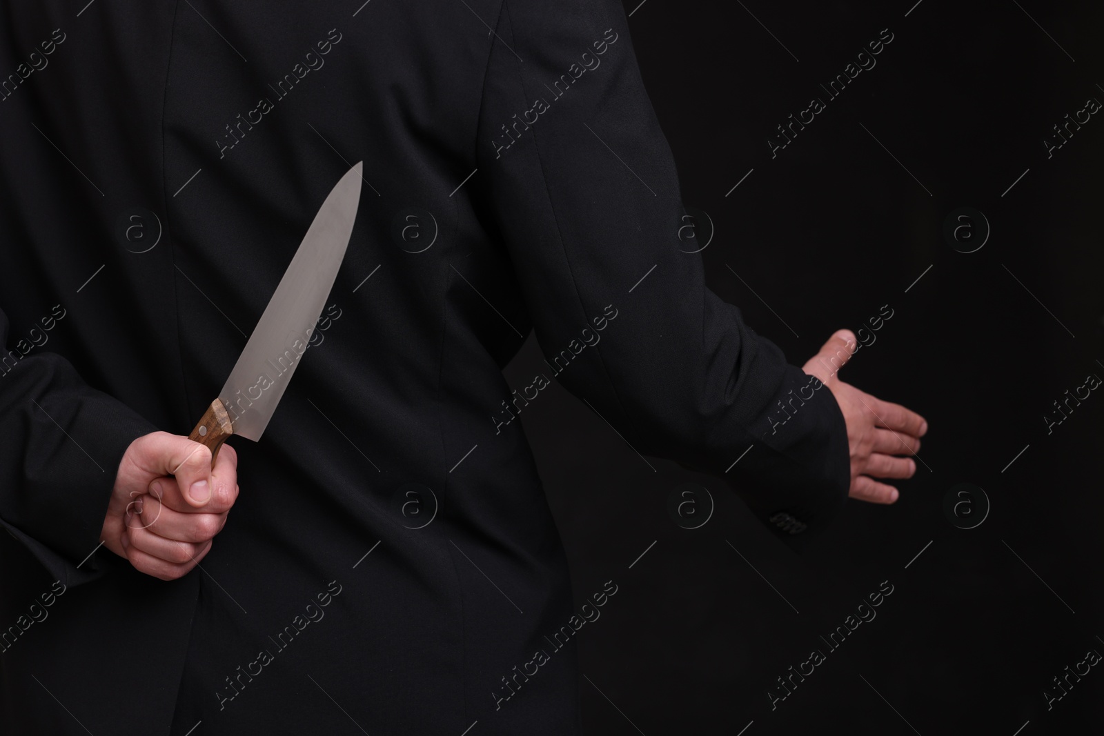 Photo of Businessman holding knife behind his back and offering handshake on black background, closeup