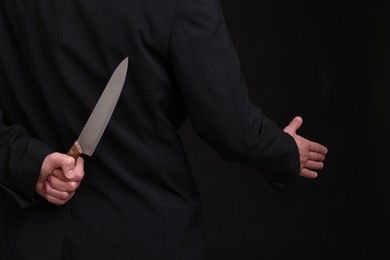 Photo of Businessman holding knife behind his back and offering handshake on black background, closeup