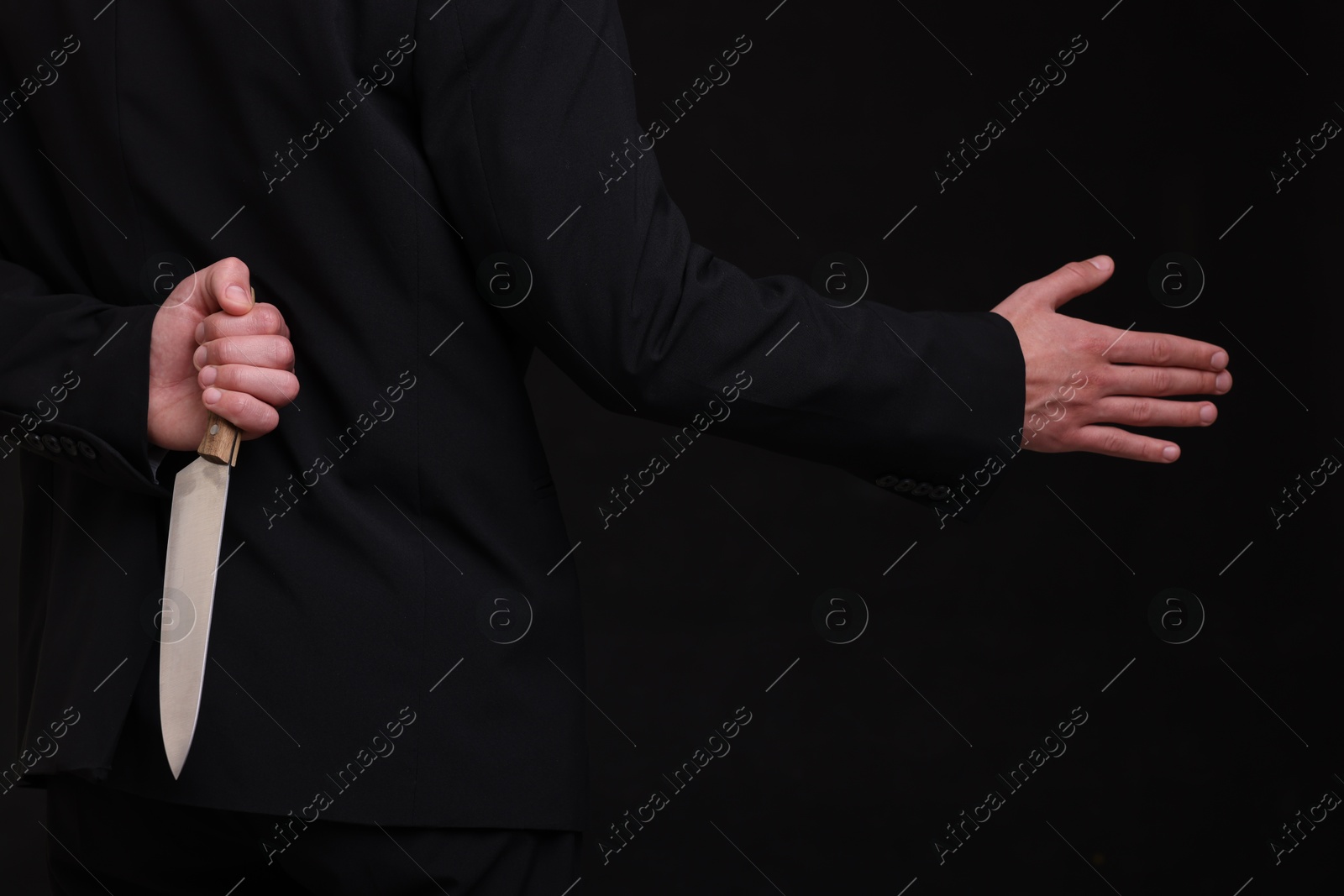 Photo of Businessman holding knife behind his back and offering handshake on black background, closeup