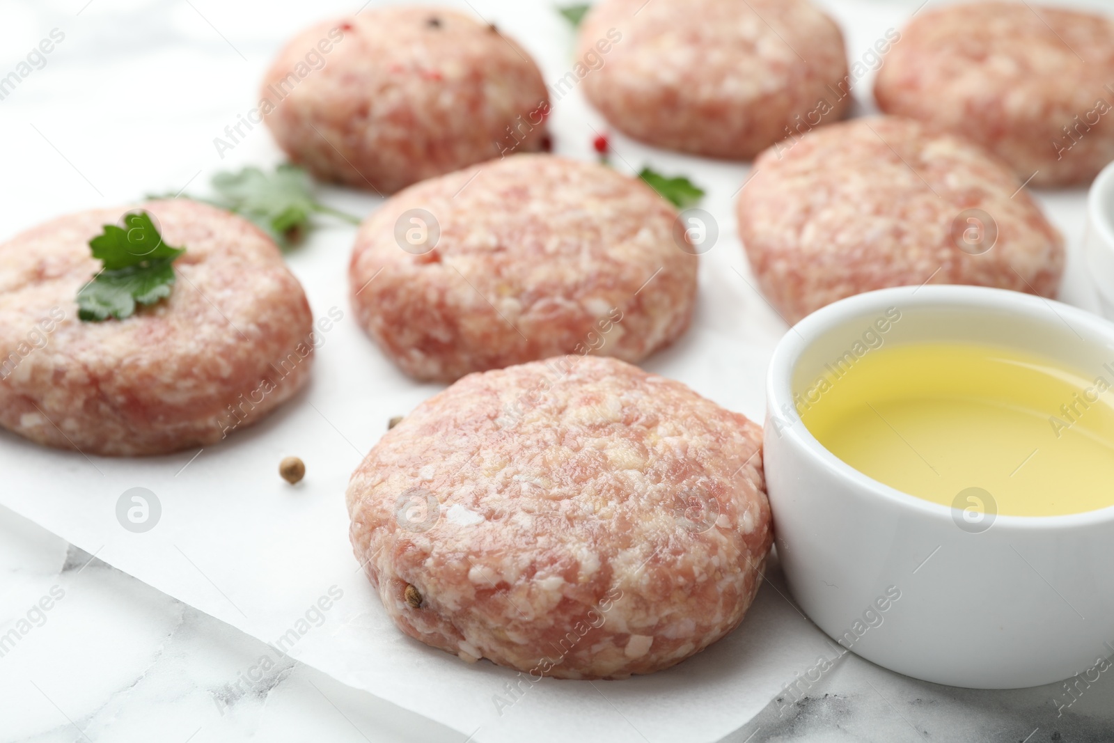 Photo of Many uncooked patties, oil and parsley on white table, closeup