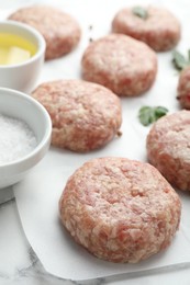 Photo of Many uncooked patties, salt, oil and parsley on white table, closeup