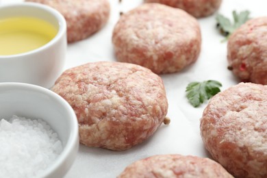 Photo of Many uncooked patties, salt, oil and parsley on white table, closeup