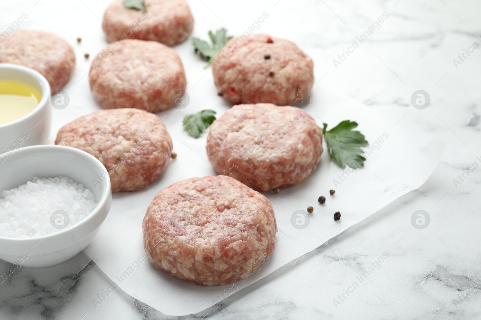 Photo of Many uncooked patties and spices on white marble table, closeup