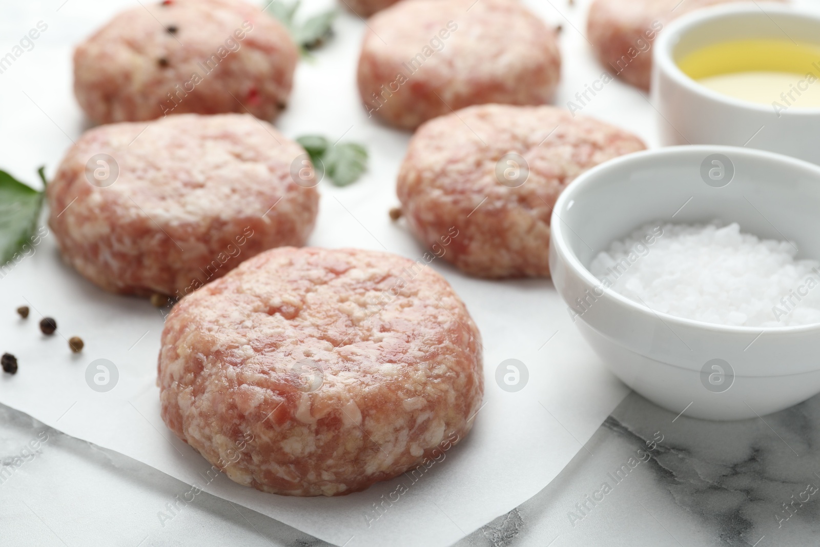 Photo of Many uncooked patties and spices on white marble table, closeup