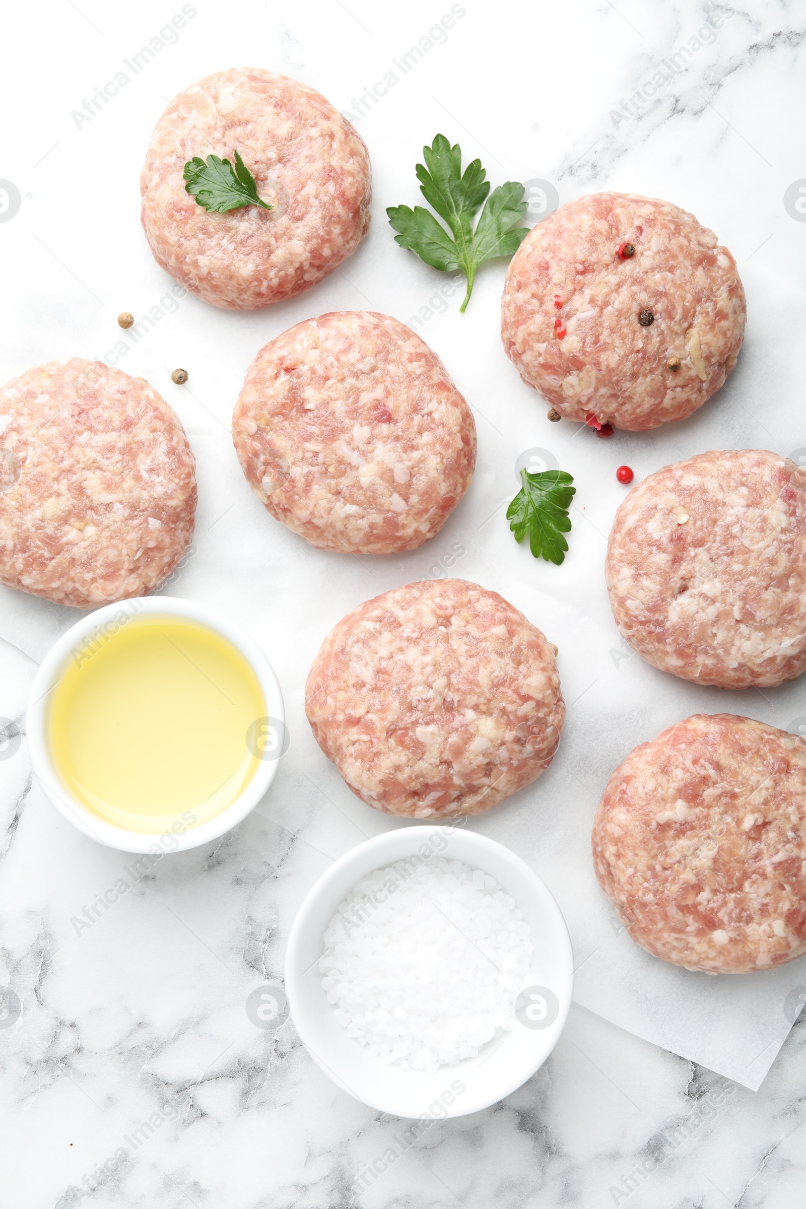 Photo of Many uncooked patties and spices on white marble table, flat lay