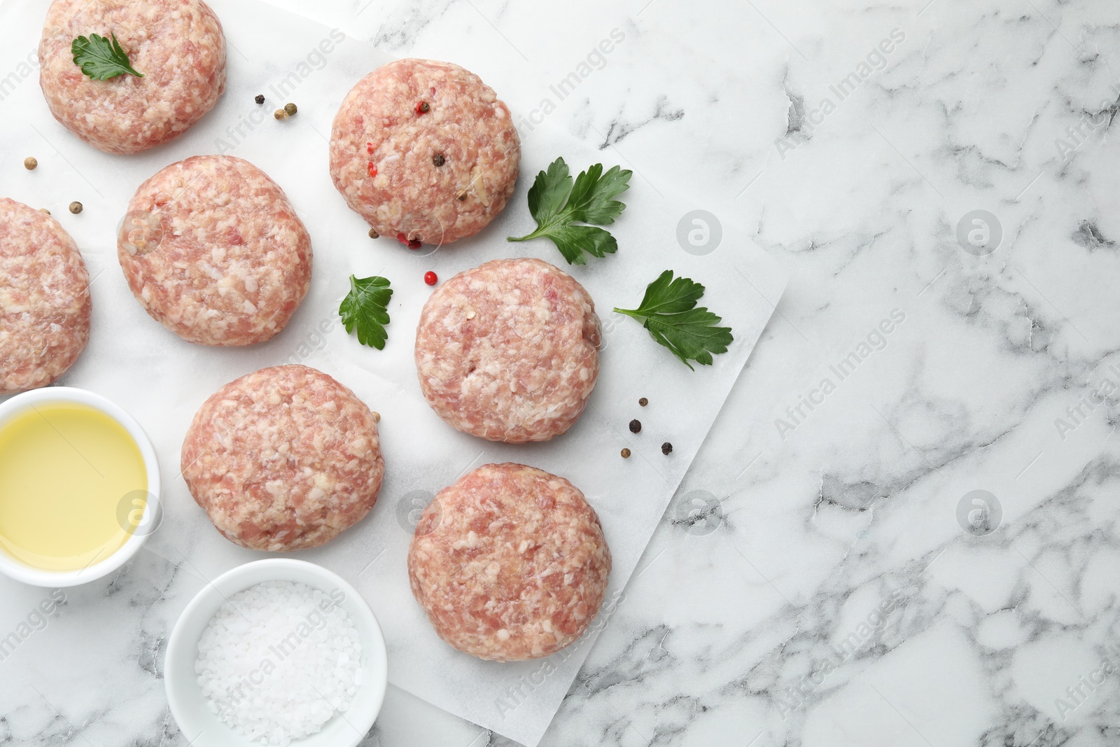 Photo of Many uncooked patties and spices on white marble table, flat lay. Space for text