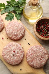 Photo of Many uncooked patties and spices on wooden table, flat lay