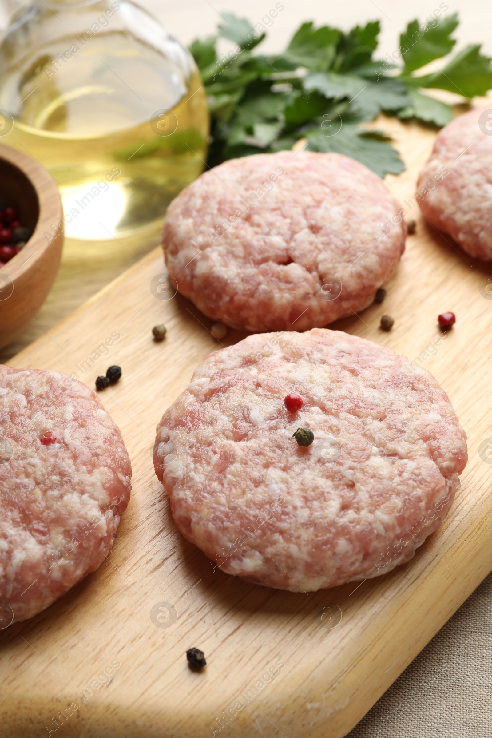 Photo of Many uncooked patties and spices on wooden table, closeup