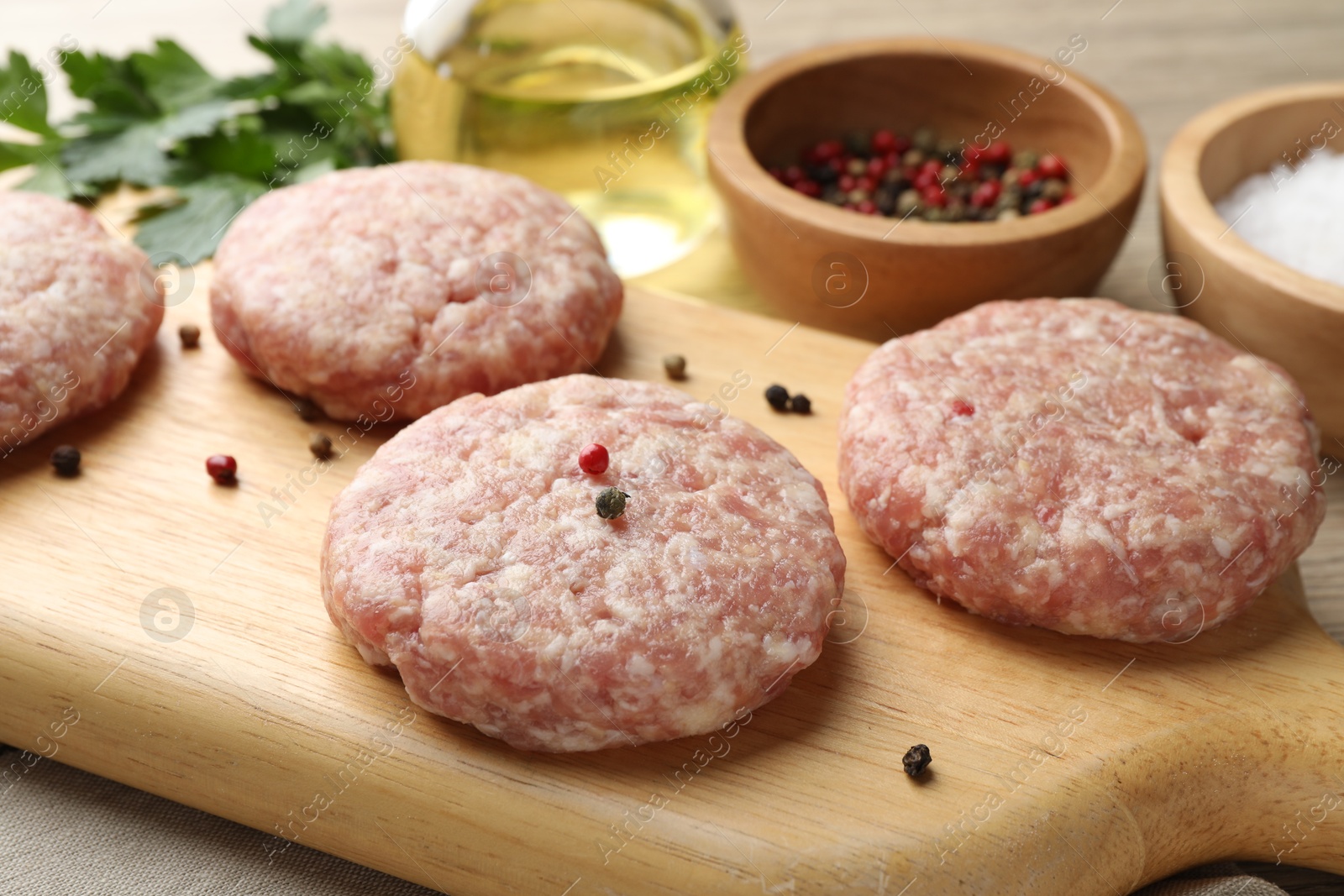 Photo of Many uncooked patties and spices on wooden table, closeup