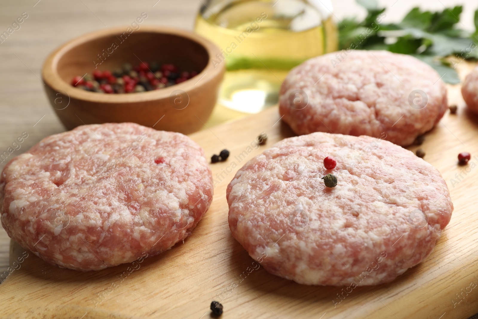 Photo of Many uncooked patties and spices on wooden table, closeup