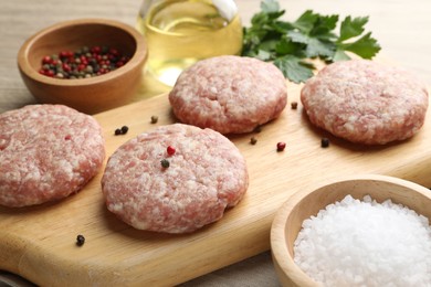 Photo of Many uncooked patties and spices on wooden table, closeup