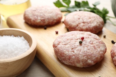 Photo of Many uncooked patties and spices on wooden table, closeup