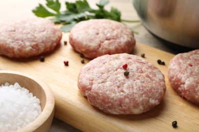 Photo of Many uncooked patties and spices on wooden table, closeup