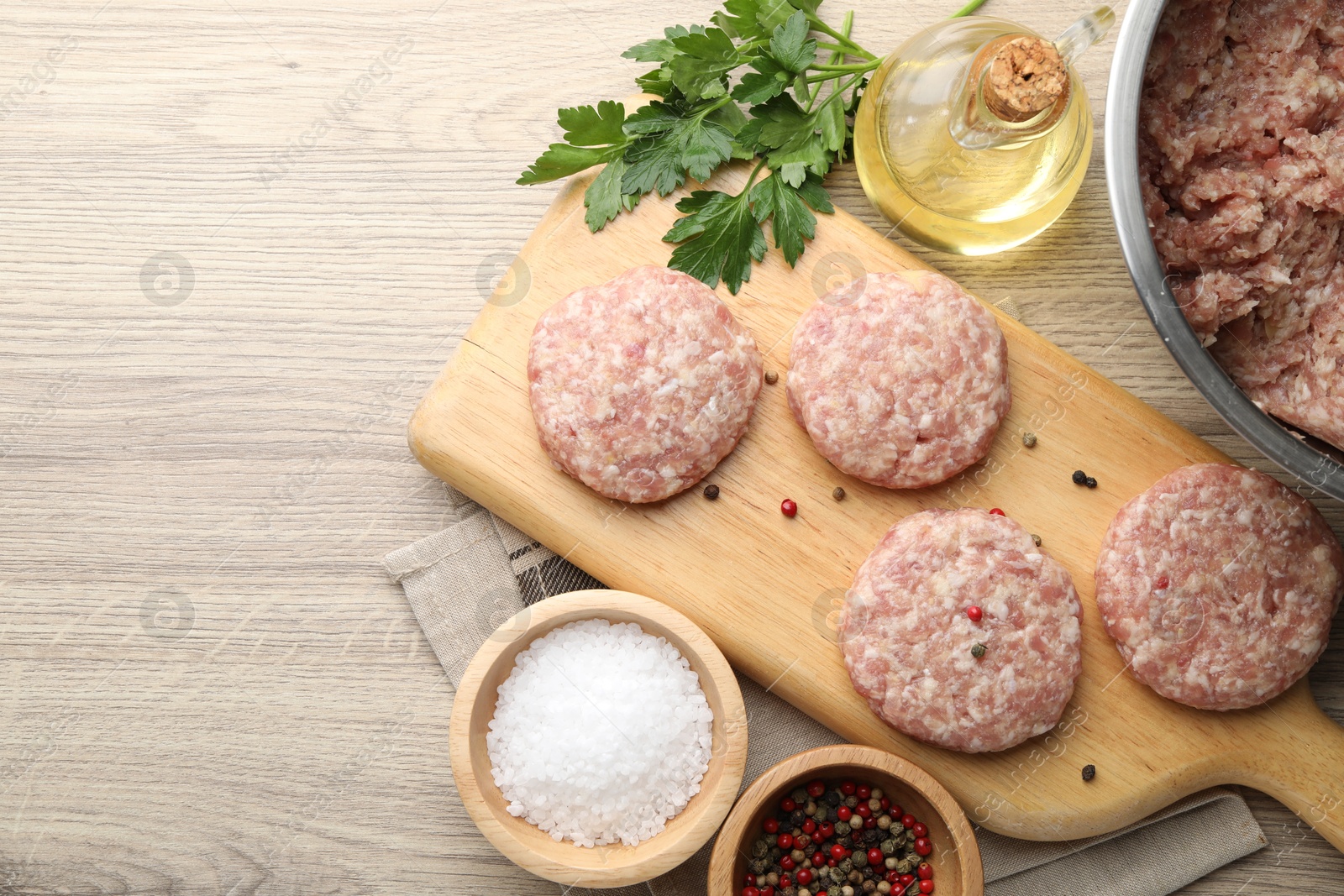 Photo of Many uncooked patties and spices on wooden table, flat lay. Space for text