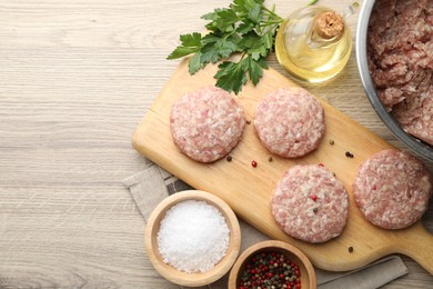 Photo of Many uncooked patties and spices on wooden table, flat lay. Space for text