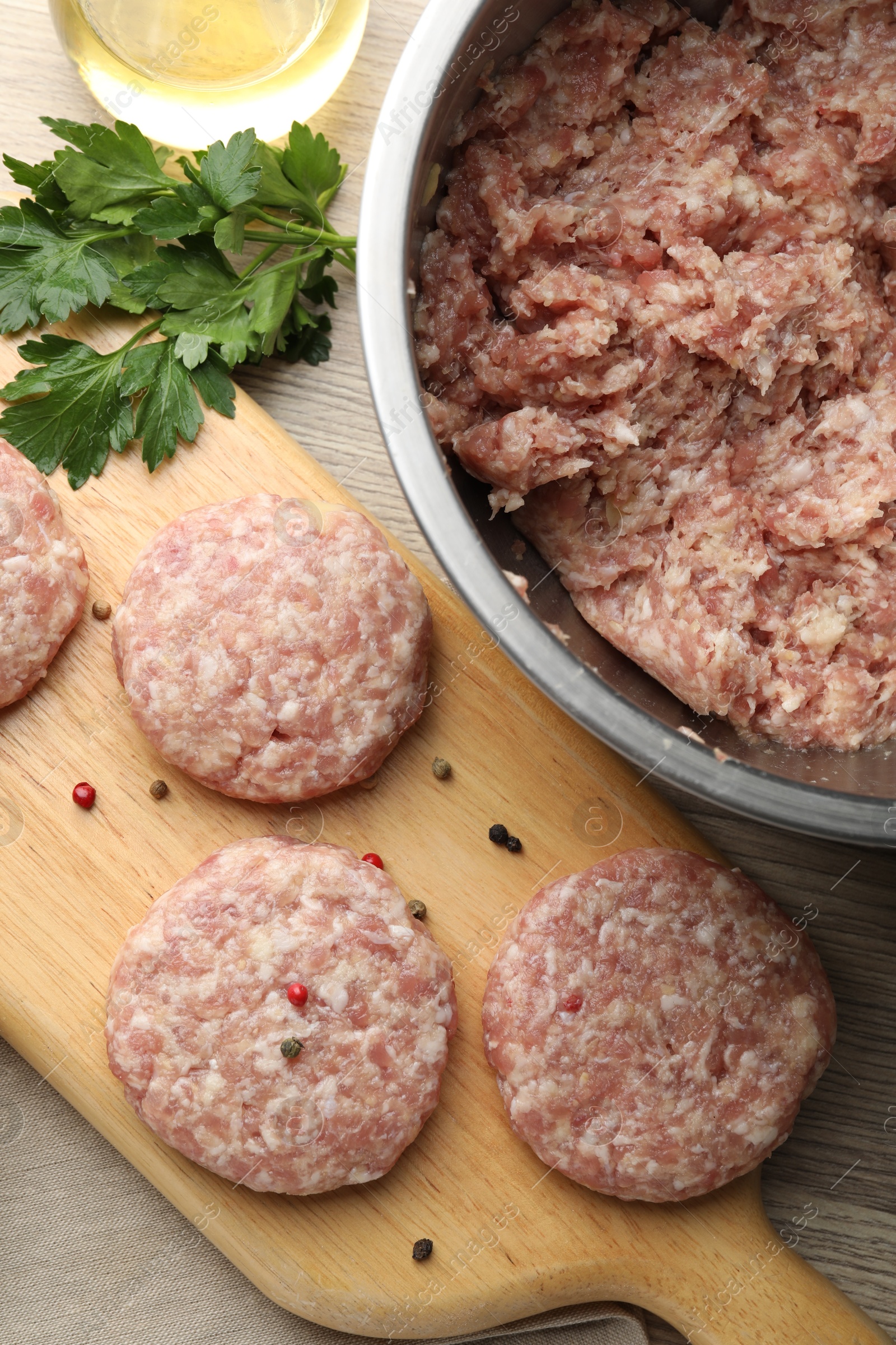 Photo of Many uncooked patties and spices on wooden table, flat lay