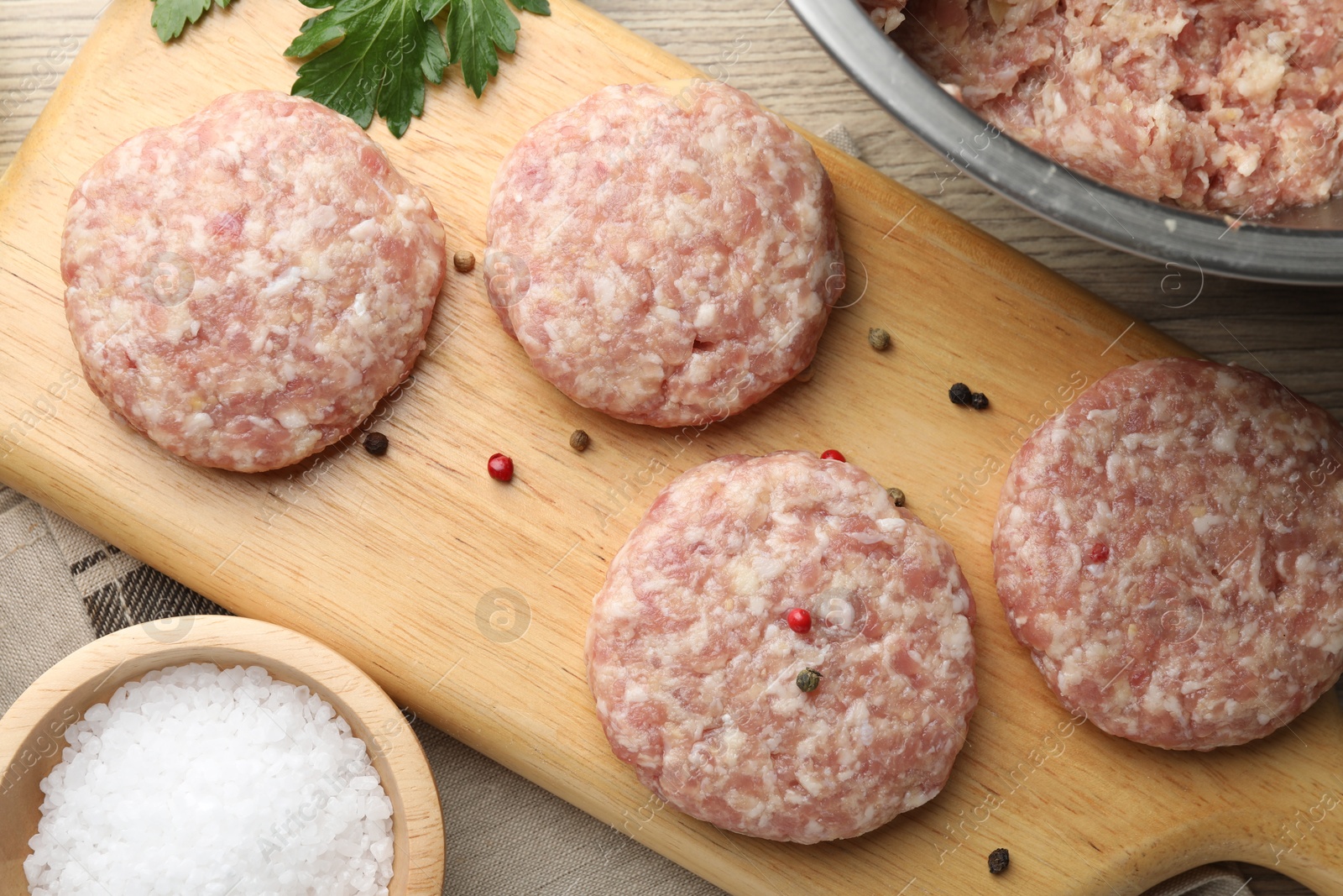 Photo of Many uncooked patties and spices on wooden table, flat lay