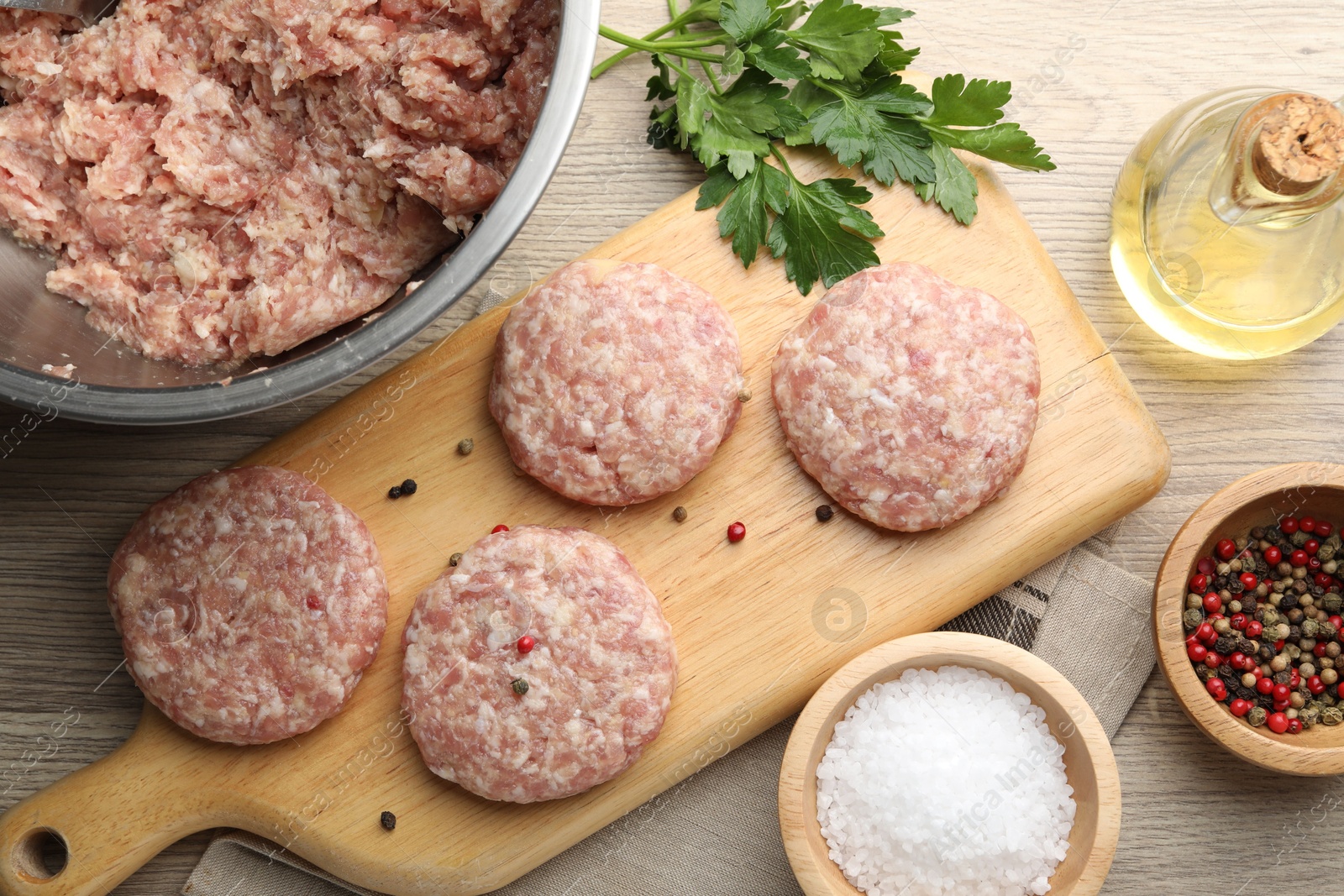 Photo of Many uncooked patties and spices on wooden table, flat lay