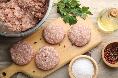 Photo of Many uncooked patties and spices on wooden table, flat lay