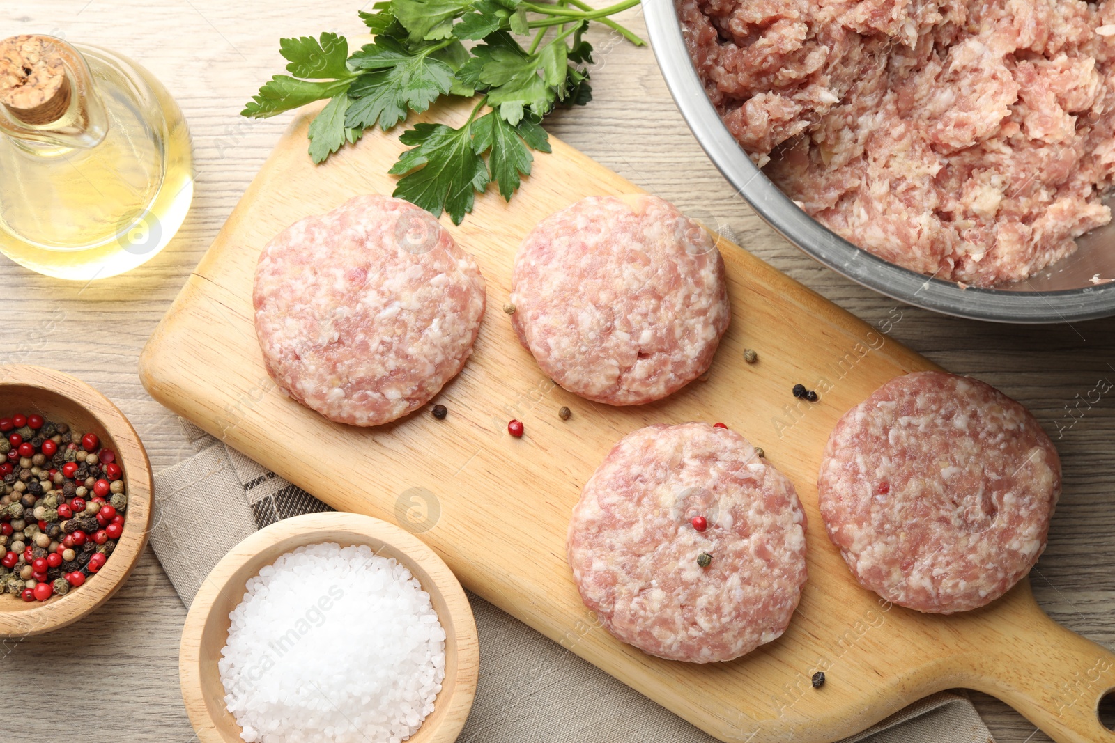 Photo of Many uncooked patties and spices on wooden table, flat lay