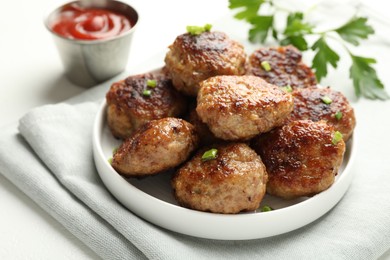 Photo of Delicious patties with green onions, parsley and ketchup on white table, closeup