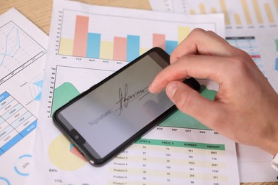 Photo of Electronic signature. Man using smartphone at table, closeup