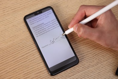 Photo of Electronic signature. Man using stylus and smartphone at wooden table, top view