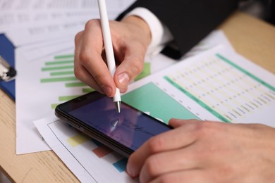 Photo of Electronic signature. Man using stylus and smartphone at wooden table, closeup