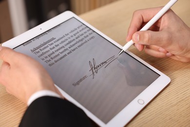 Photo of Electronic signature. Man using stylus and tablet at wooden table, closeup