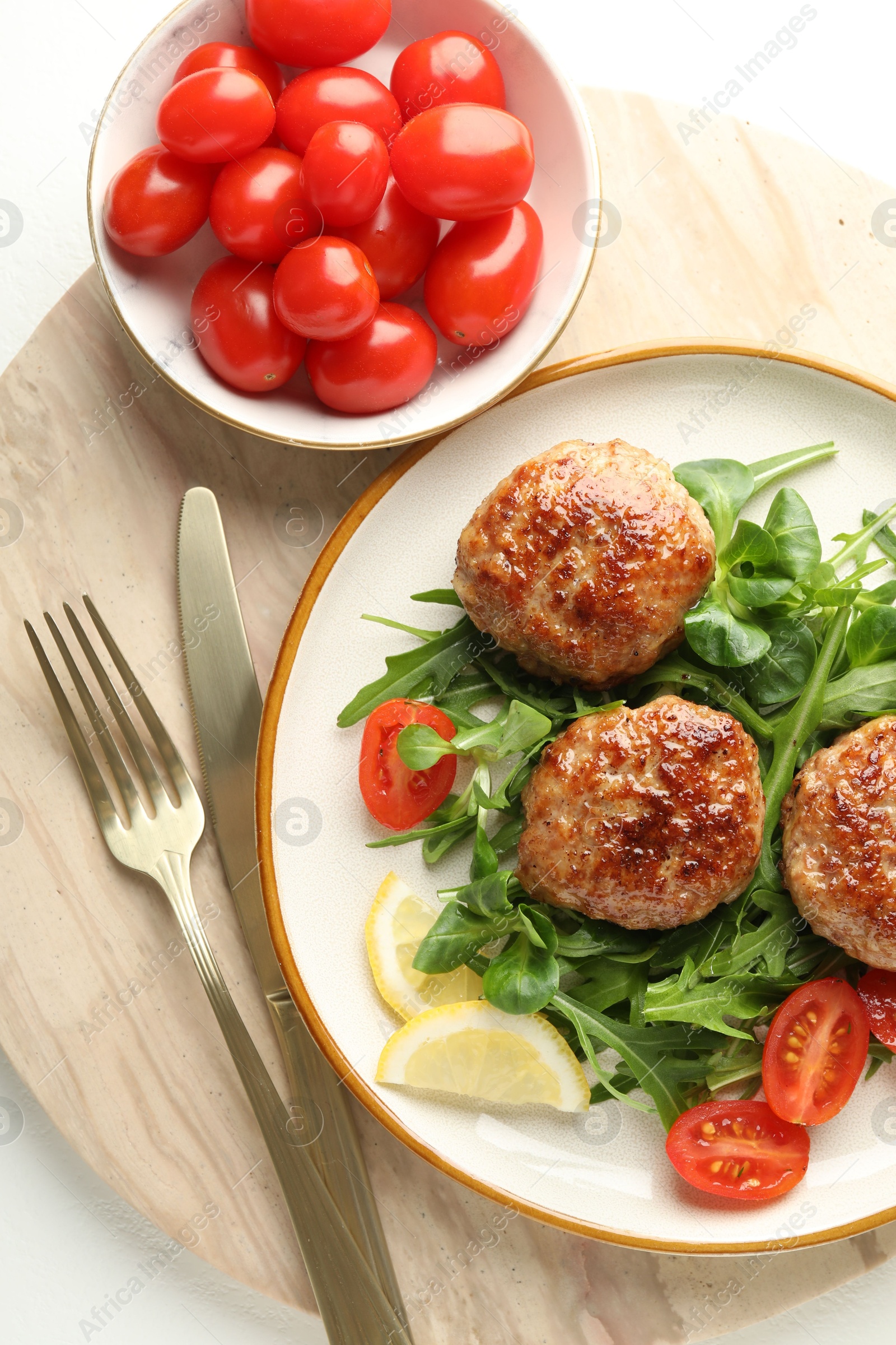 Photo of Delicious patties with greens, tomatoes and cutlery on white table, top view