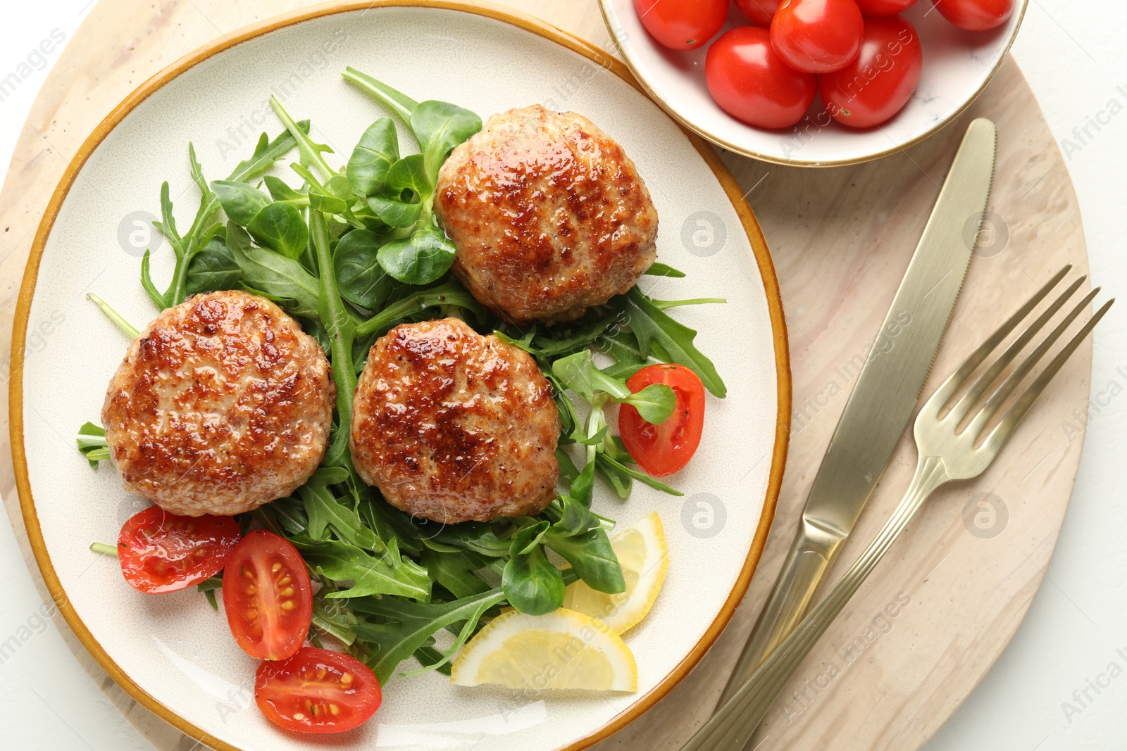 Photo of Delicious patties with greens, tomatoes and cutlery on white table, top view