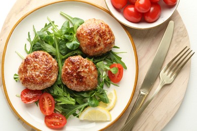 Photo of Delicious patties with greens, tomatoes and cutlery on white table, top view