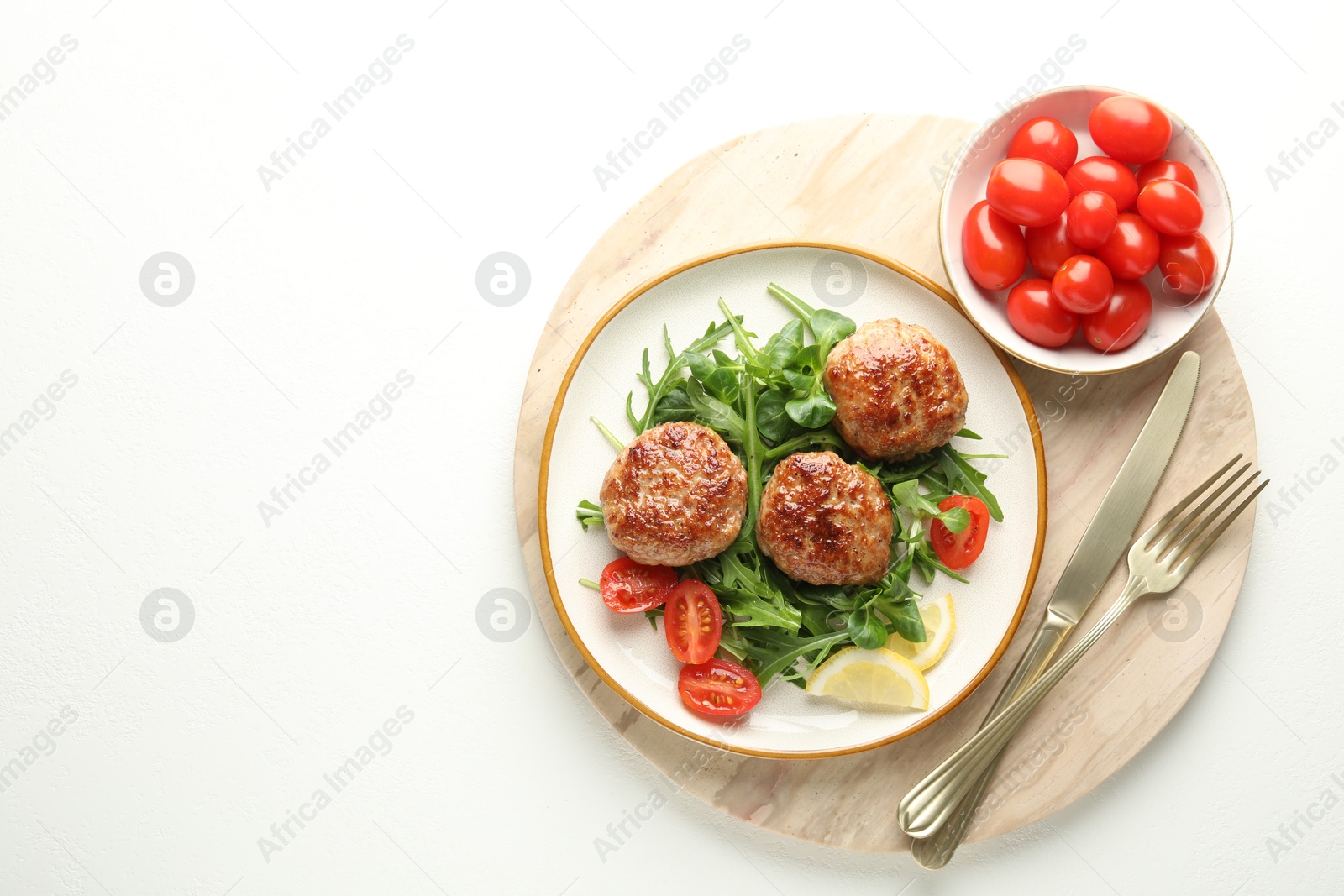 Photo of Delicious patties with greens, tomatoes and cutlery on white table, top view. Space for text