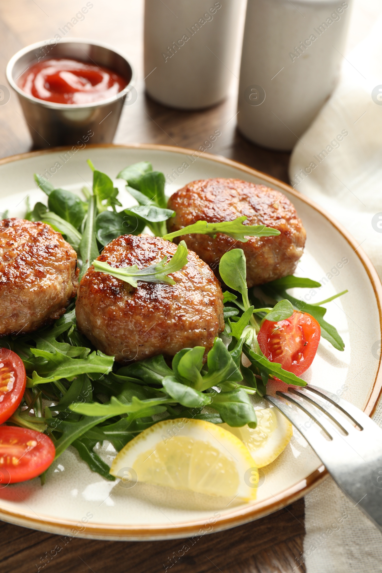 Photo of Delicious patties with greens, tomatoes and ketchup on wooden table, closeup