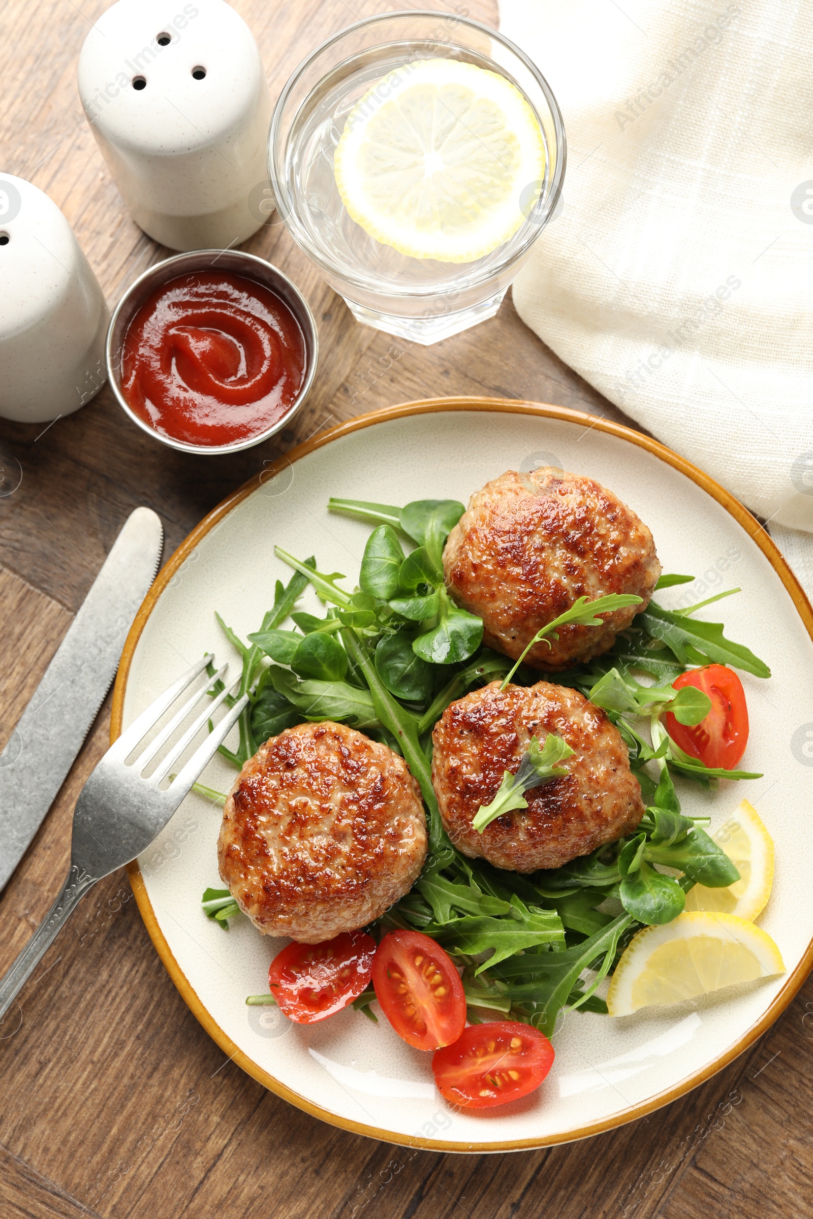 Photo of Delicious patties with greens, tomatoes, ketchup and drink on wooden table, flat lay