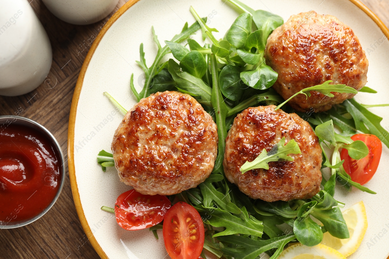 Photo of Delicious patties with greens, tomatoes and ketchup on wooden table, flat lay