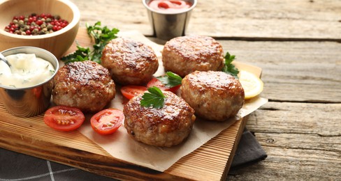 Photo of Delicious patties, spices, tomatoes and sauces on wooden table, closeup. Space for text