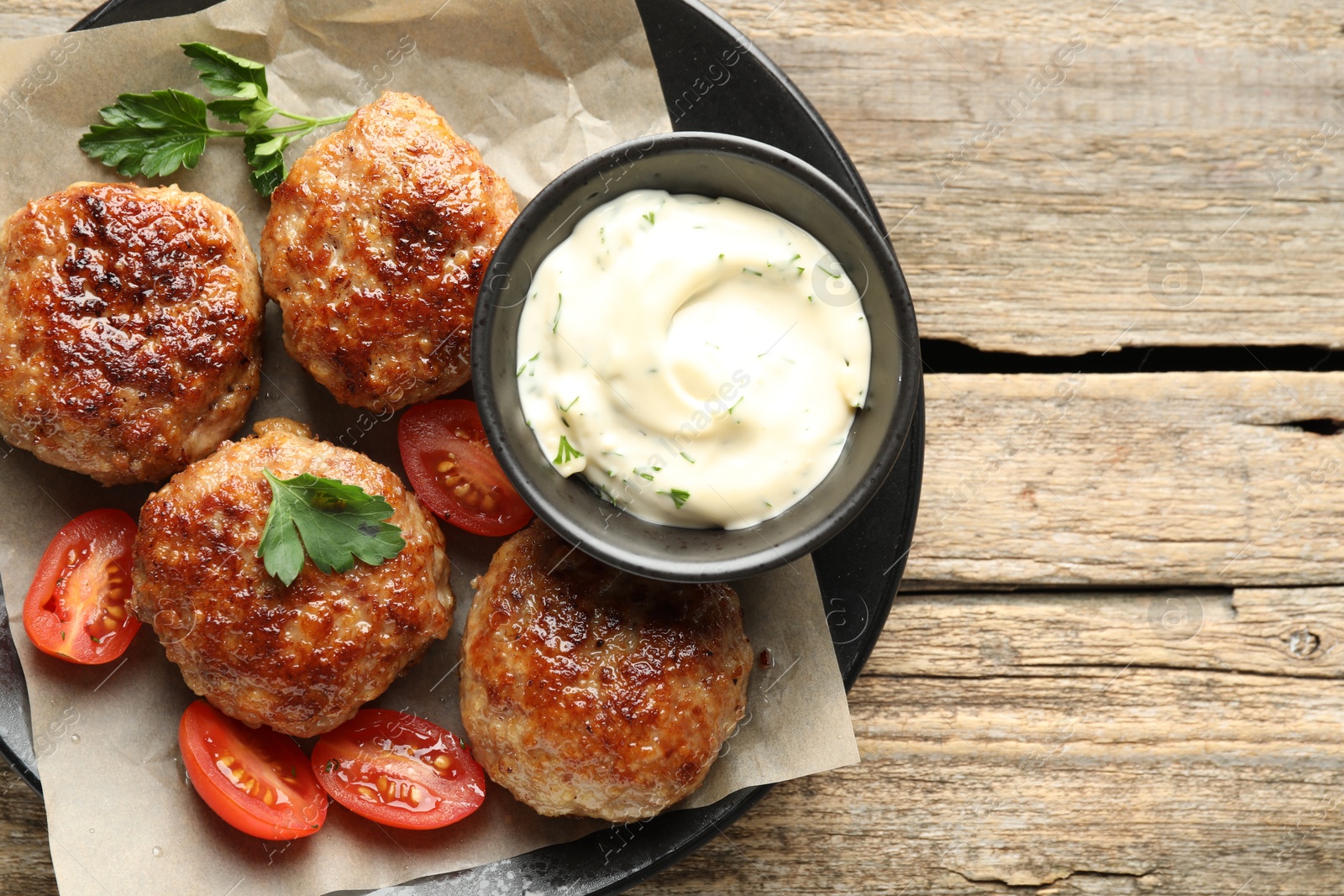 Photo of Delicious patties, parsley, tomatoes and sauce on wooden table, top view. Space for text