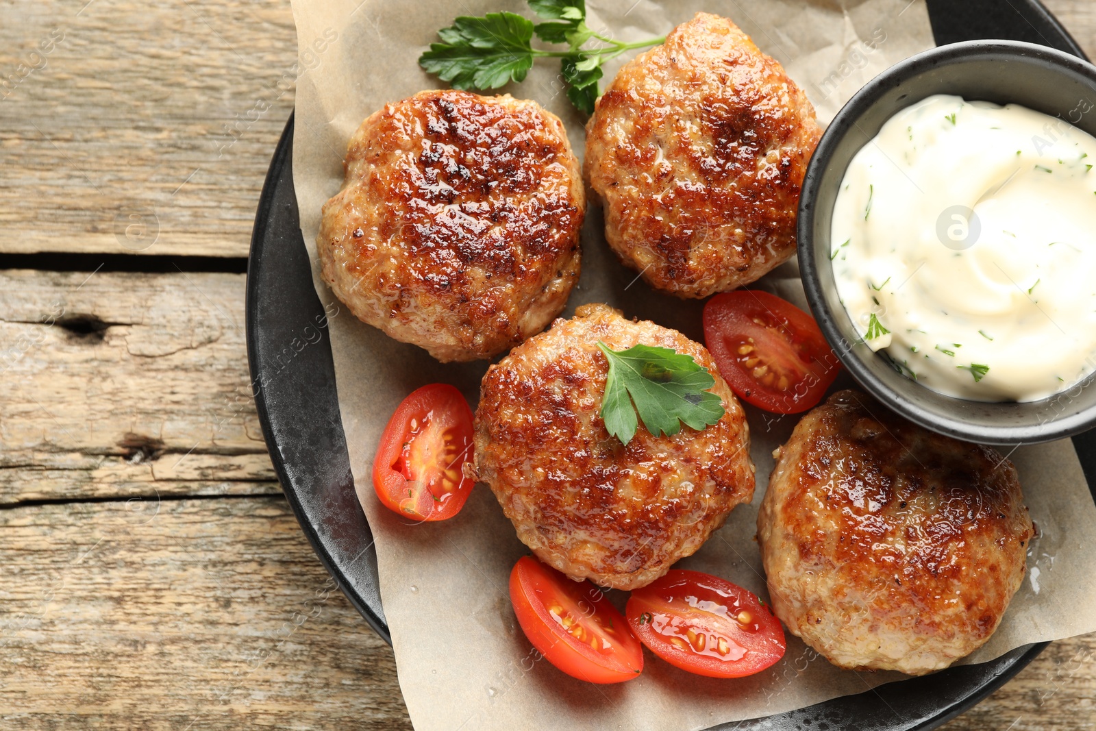 Photo of Delicious patties, parsley, tomatoes and sauce on wooden table, top view. Space for text