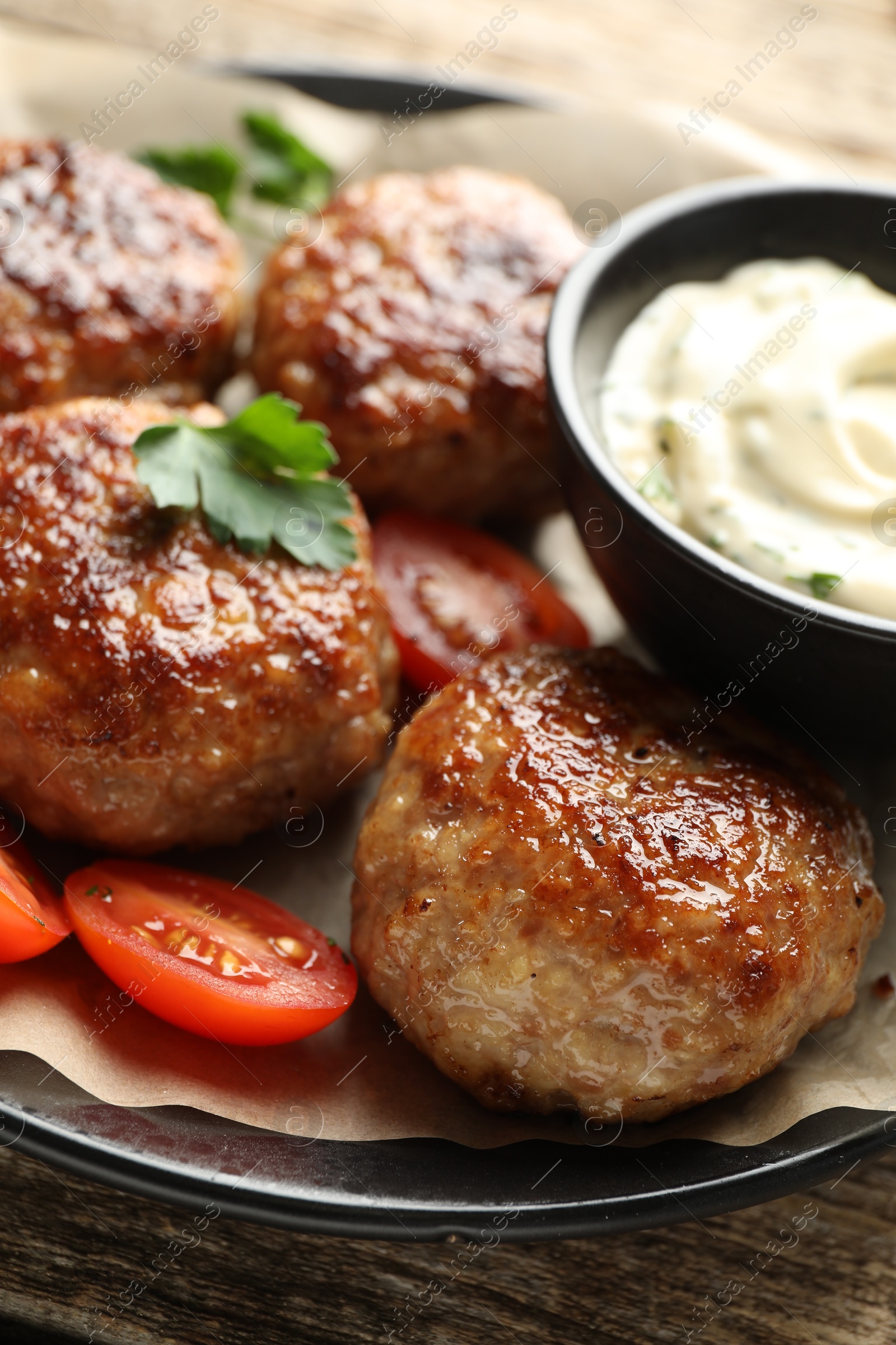 Photo of Delicious patties, parsley, tomatoes and sauce on wooden table, closeup