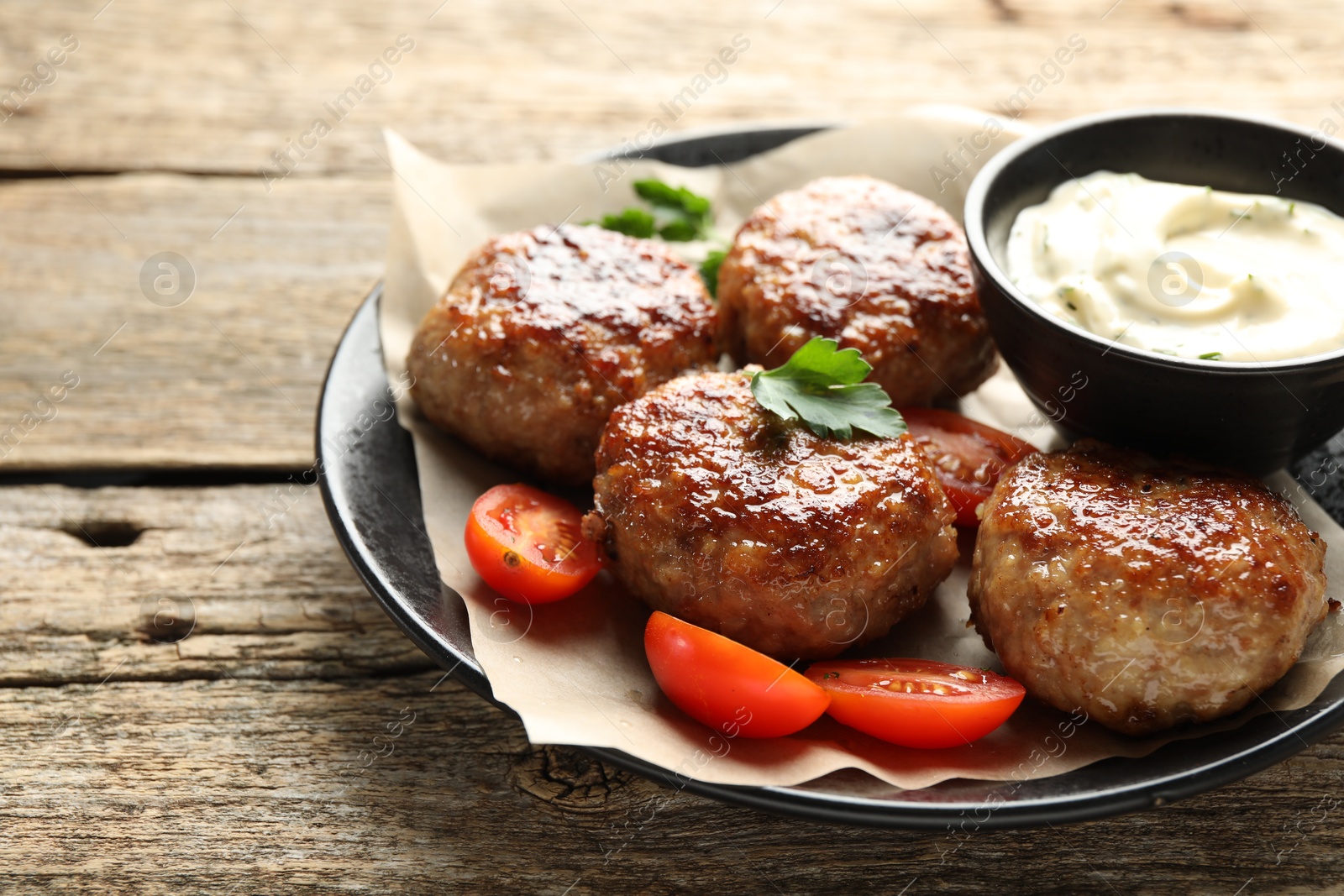 Photo of Delicious patties, parsley, tomatoes and sauce on wooden table, closeup. Space for text